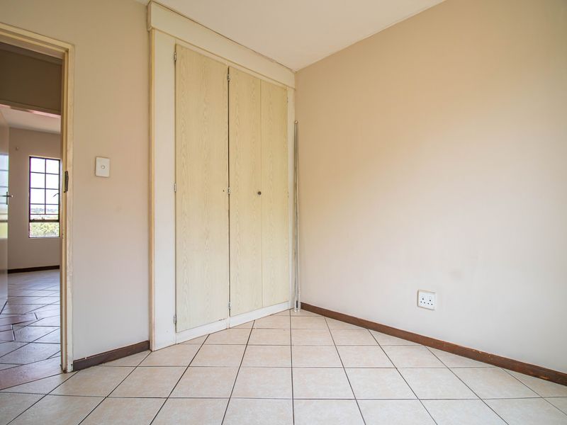 An empty bedroom featuring neutral tiled flooring, built-in cupboards, and access to an adjacent hallway.