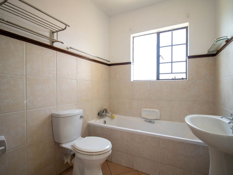 A functional bathroom featuring a bathtub, pedestal basin, and toilet with neutral wall tiling and natural light from a window.