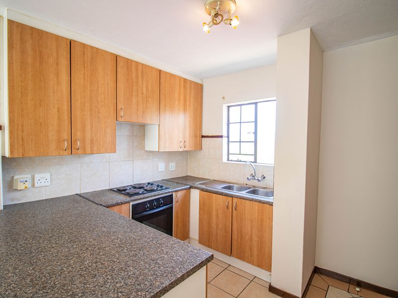 A functional kitchen featuring laminate cabinetry, a built-in electric oven and hob, double stainless steel sink, and tiled backsplash.