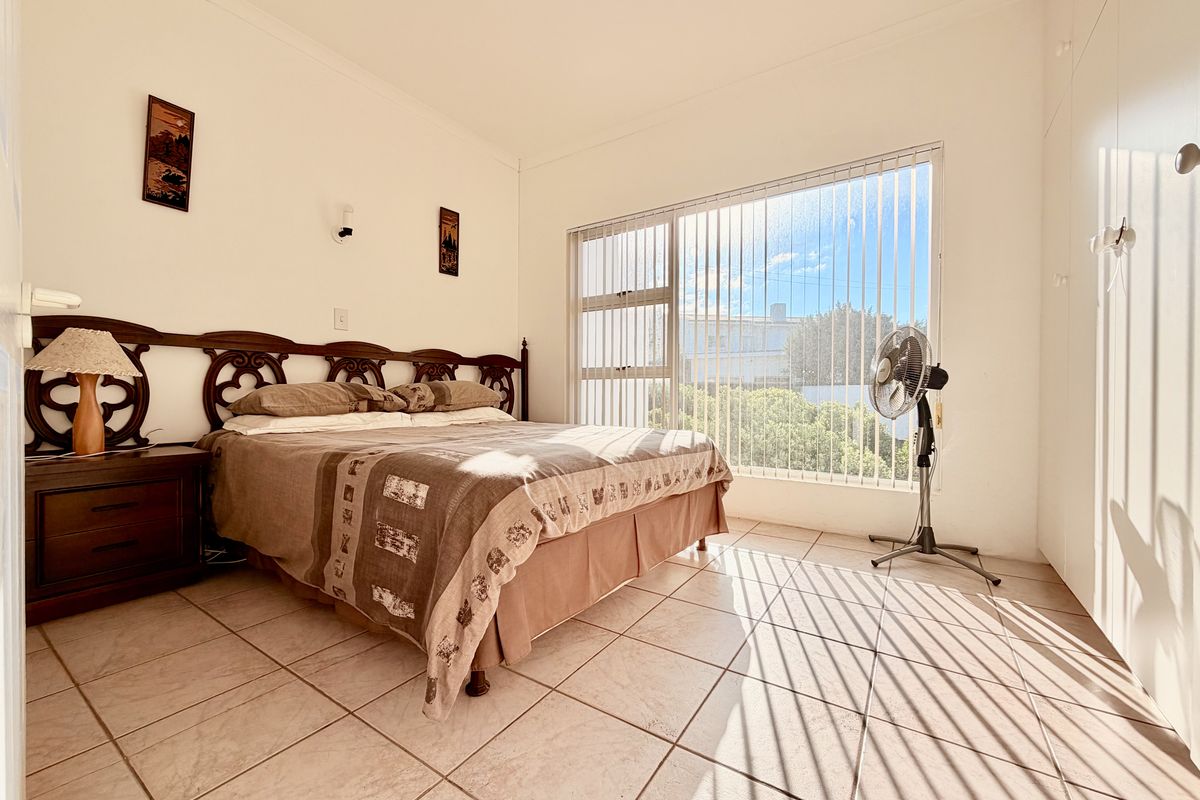 A bright bedroom featuring tiled flooring, built-in cupboards, and a large window with vertical blinds allowing for ample natural light.