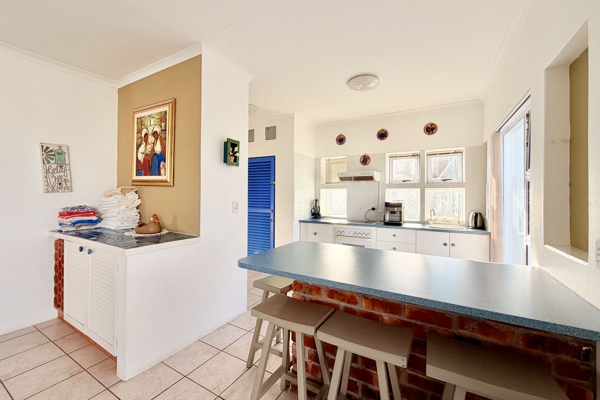 A functional kitchen featuring a brick-based breakfast bar, tiled flooring, built-in cabinetry, and an integrated extractor fan with natural light from multiple windows.