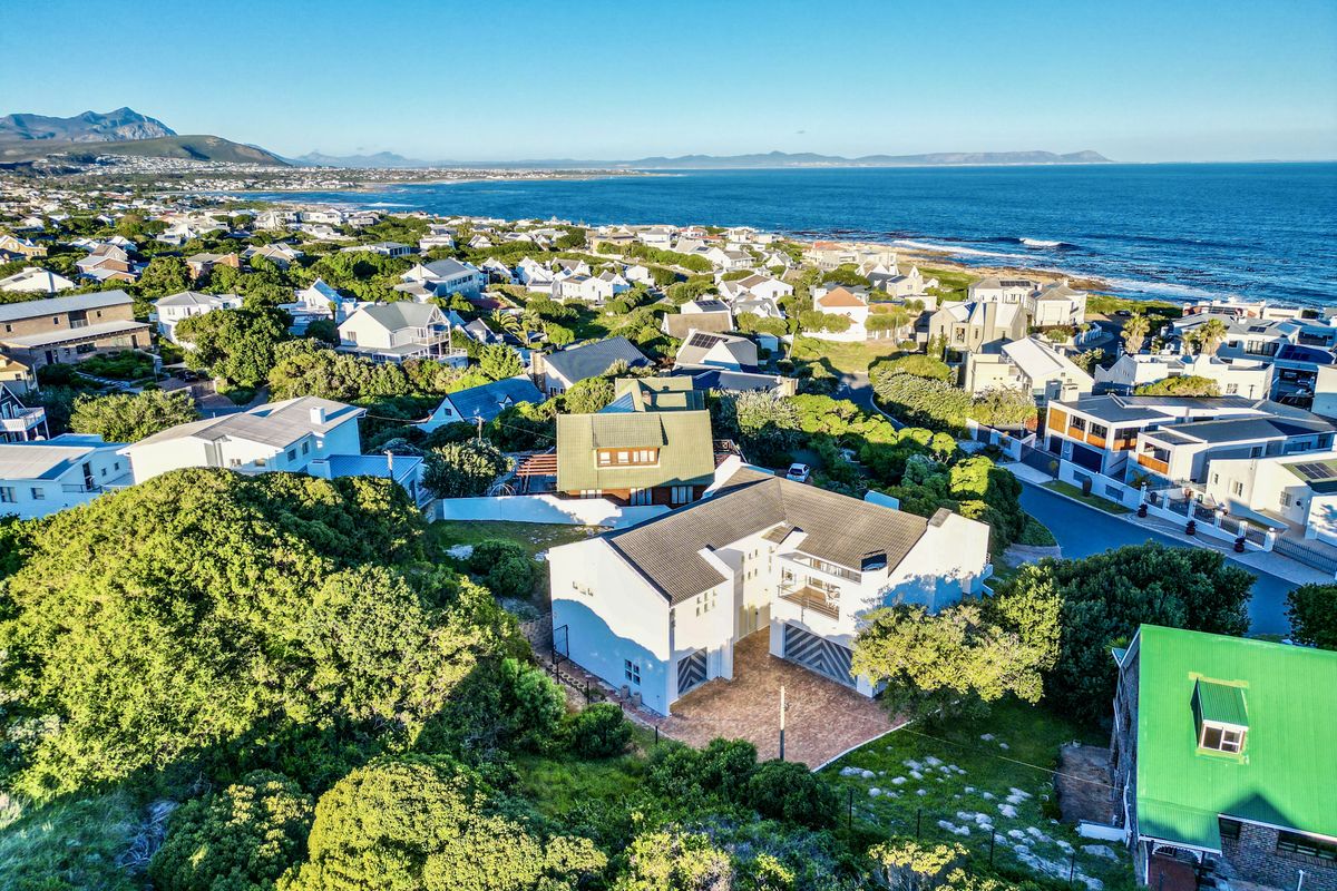 Aerial view of a coastal residential property featuring a tiled roof, paved driveway, and double garage, situated in a scenic seaside neighborhood.