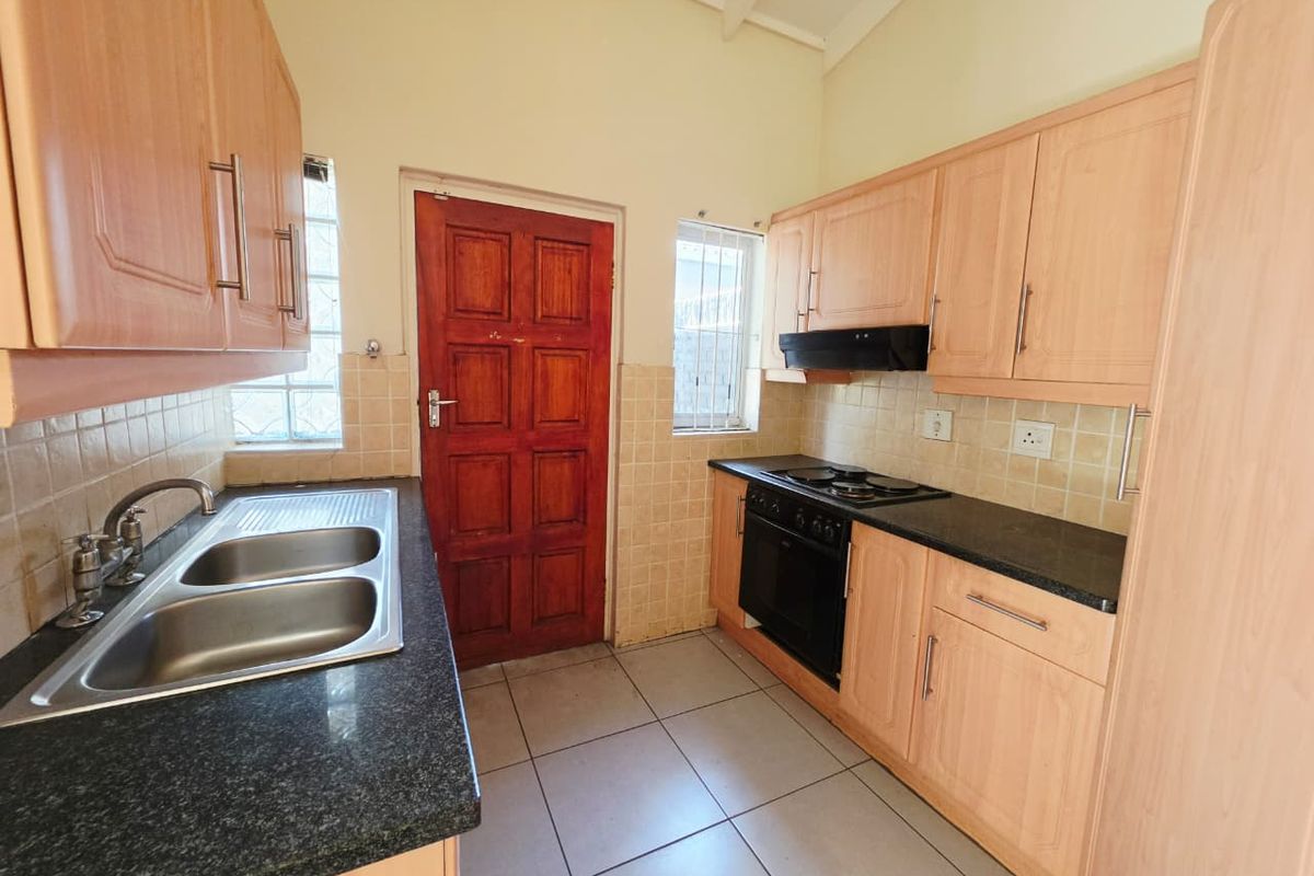 A functional kitchen featuring light wood cabinetry, granite countertops, a double sink, and built-in oven with hob, finished with tiled flooring and backsplash.