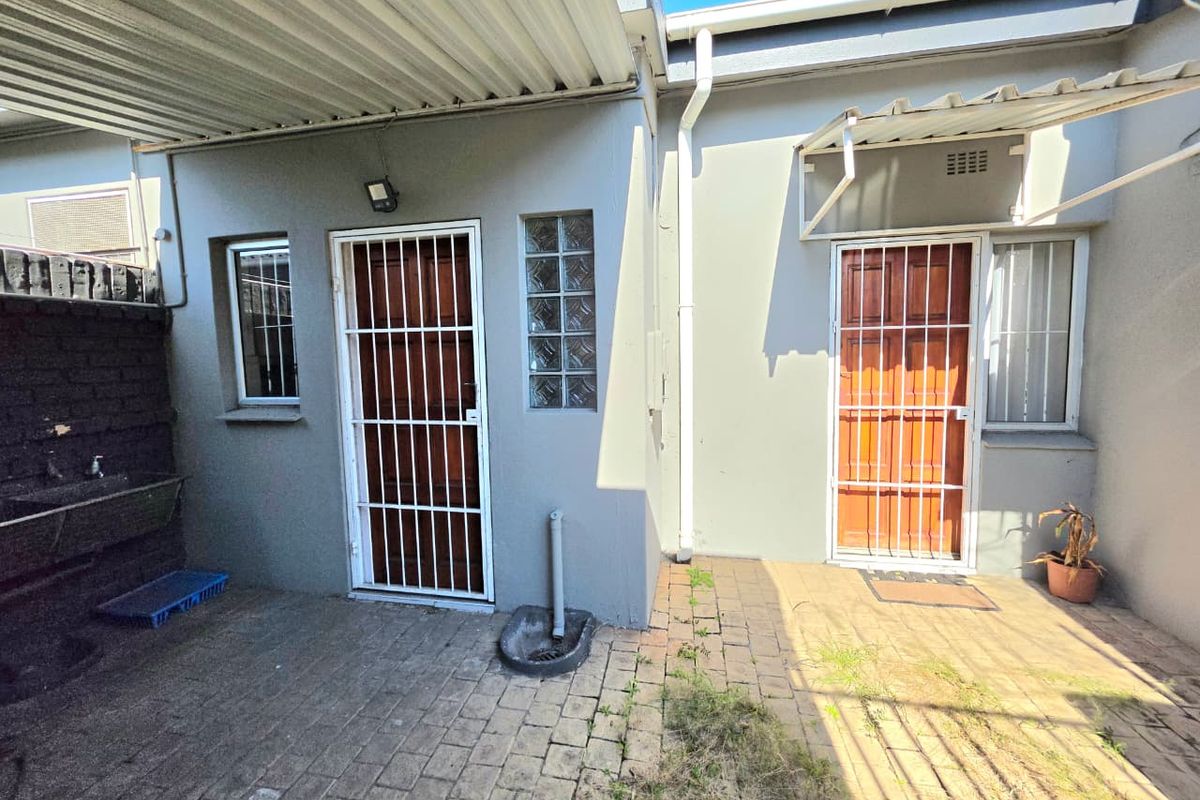 Rear exterior courtyard featuring paved flooring, security gates, an external utility sink, and a covered section with corrugated metal roofing.