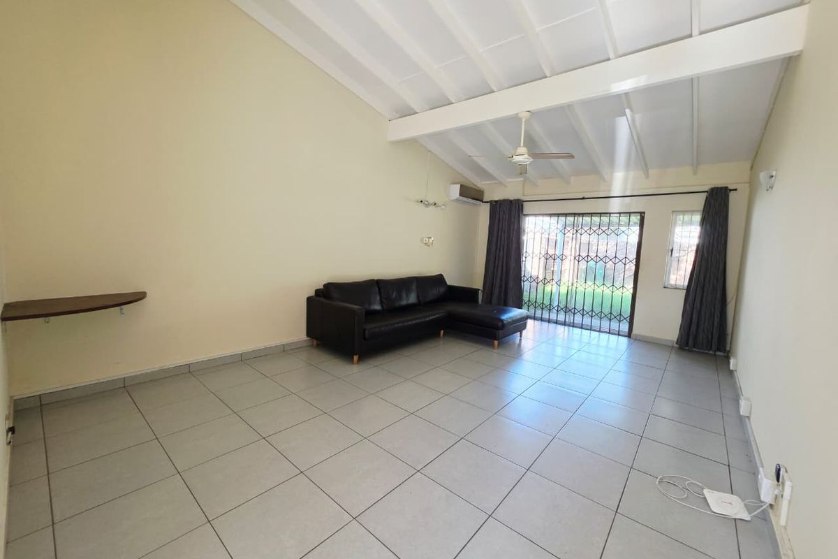 Spacious living area featuring vaulted ceilings with exposed beams, tiled flooring, air conditioning, and direct access to the outdoor area through a security gate.