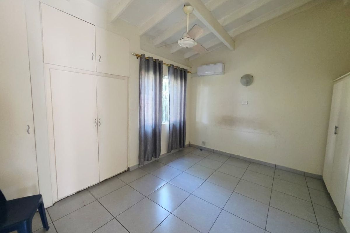 A spacious bedroom featuring tiled flooring, built-in cupboards, a ceiling fan, and a split-system air conditioner, offering a blank canvas for personalization.