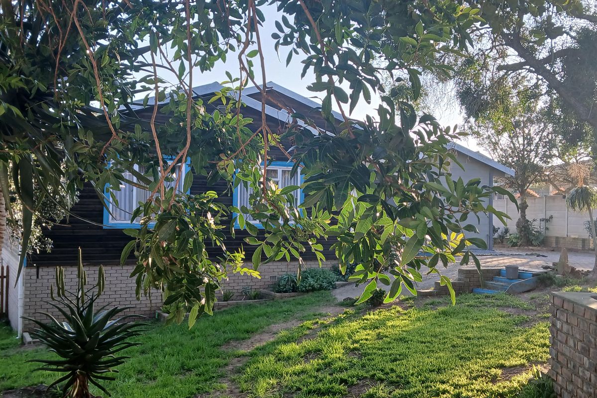 Rear view of the property featuring timber cladding, brick foundation, and a landscaped garden area with mature trees.