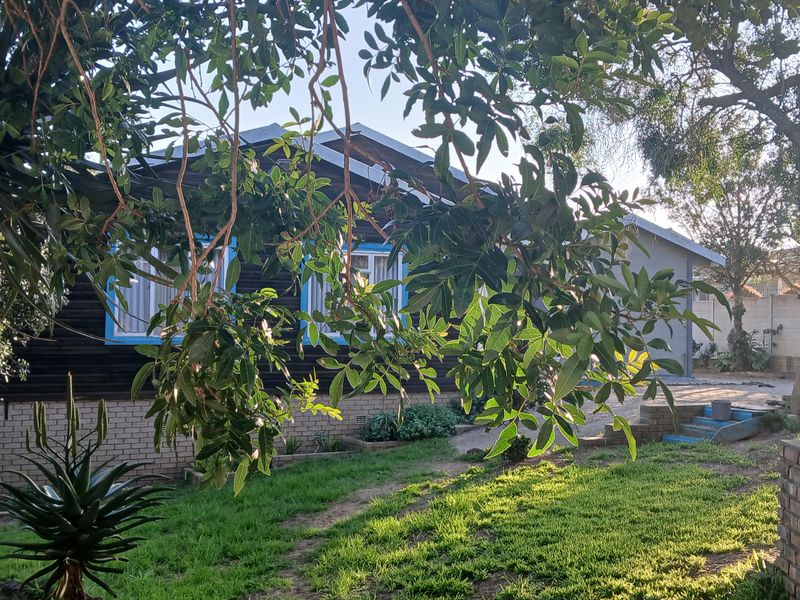 Rear view of the property featuring timber cladding, brick foundation, and a landscaped garden area with mature trees.