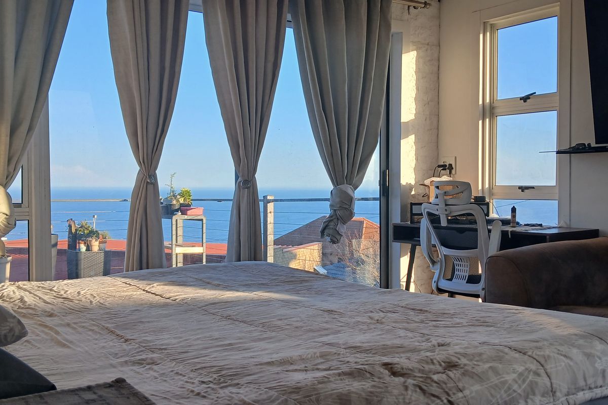A bright bedroom featuring large glass sliding doors that open to an expansive ocean view, complemented by an exposed brick wall.