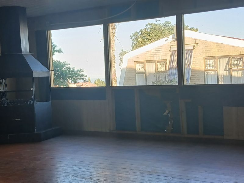 Spacious living area featuring a freestanding fireplace, timber flooring, and large windows, currently requiring wall repairs and finishing.