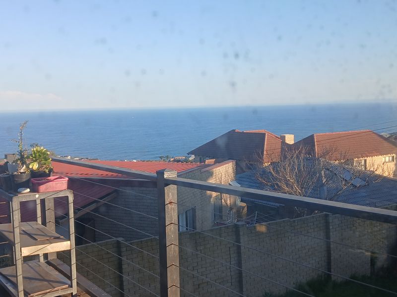 A scenic elevated view overlooking the ocean and surrounding residential neighborhood, captured through a window with a stainless steel cable railing in the foreground.