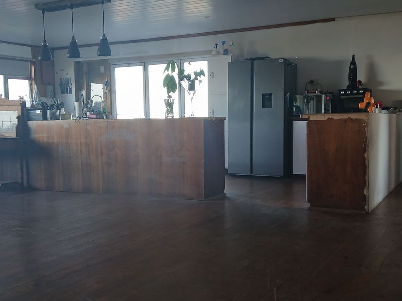 Spacious open-plan living and kitchen area featuring timber flooring, a central island, and pendant lighting, offering significant potential for renovation and modernization.