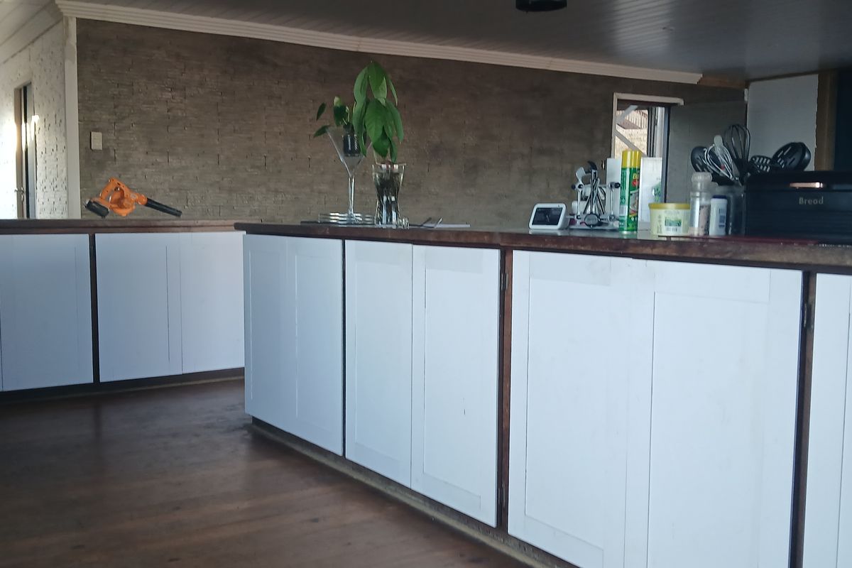 Kitchen area featuring a central island with timber countertops, white cabinetry, and an exposed brick feature wall, set against timber flooring.