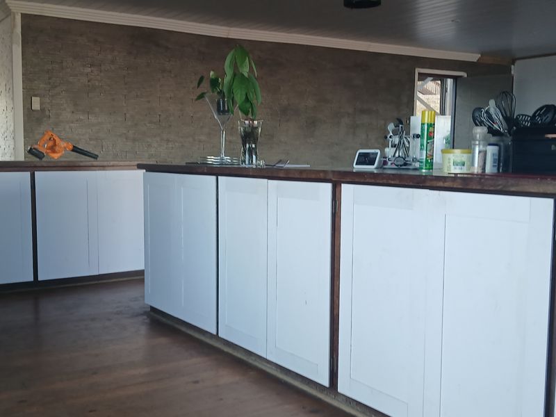 Kitchen area featuring a central island with timber countertops, white cabinetry, and an exposed brick feature wall, set against timber flooring.