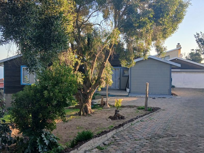 Front view of the property featuring a paved driveway, garage, and mature garden landscaping with timber-clad exterior walls.
