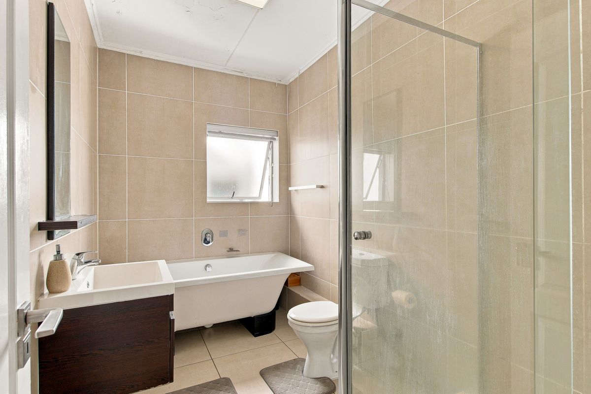 A functional bathroom featuring a freestanding bathtub, separate glass-enclosed shower, vanity cabinet, and neutral ceramic tiling throughout.