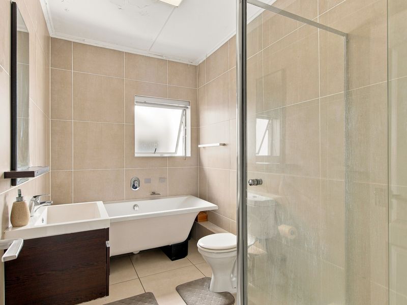 A functional bathroom featuring a freestanding bathtub, separate glass-enclosed shower, vanity cabinet, and neutral ceramic tiling throughout.