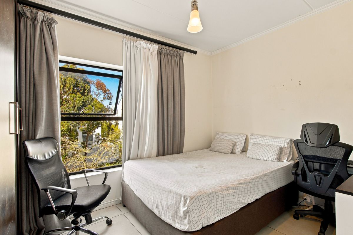 A functional bedroom featuring tiled flooring, a top-hung window with natural light, and a built-in wardrobe.