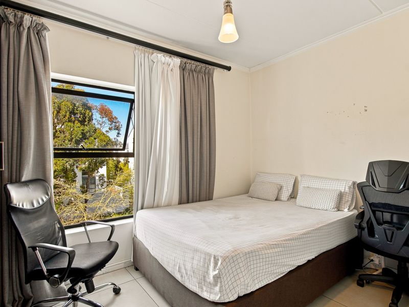 A functional bedroom featuring tiled flooring, a top-hung window with natural light, and a built-in wardrobe.
