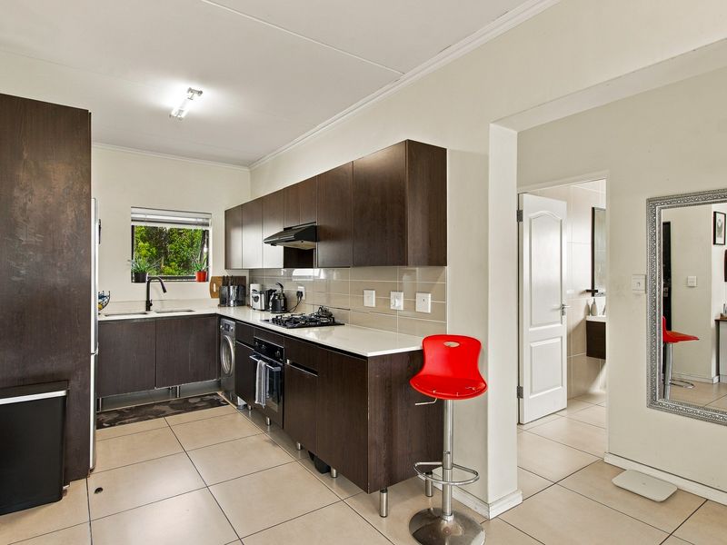 Modern kitchen featuring dark wood cabinetry, built-in oven, gas hob, extractor fan, and tiled flooring, with an adjacent hallway leading to the bathroom.