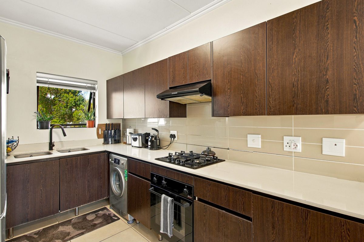 Modern kitchen featuring dark wood cabinetry, stone countertops, gas hob, built-in oven, extractor fan, and tiled backsplash with integrated laundry appliance space.
