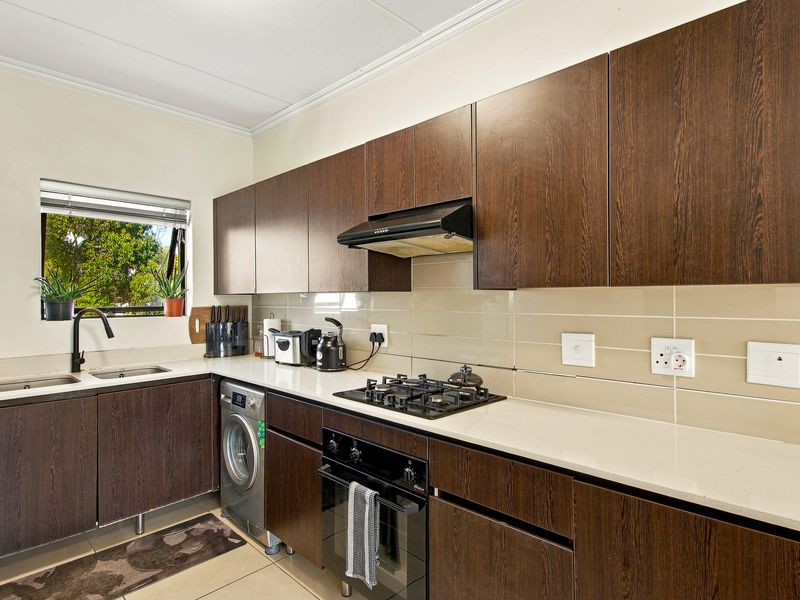 Modern kitchen featuring dark wood cabinetry, stone countertops, gas hob, built-in oven, extractor fan, and tiled backsplash with integrated laundry appliance space.