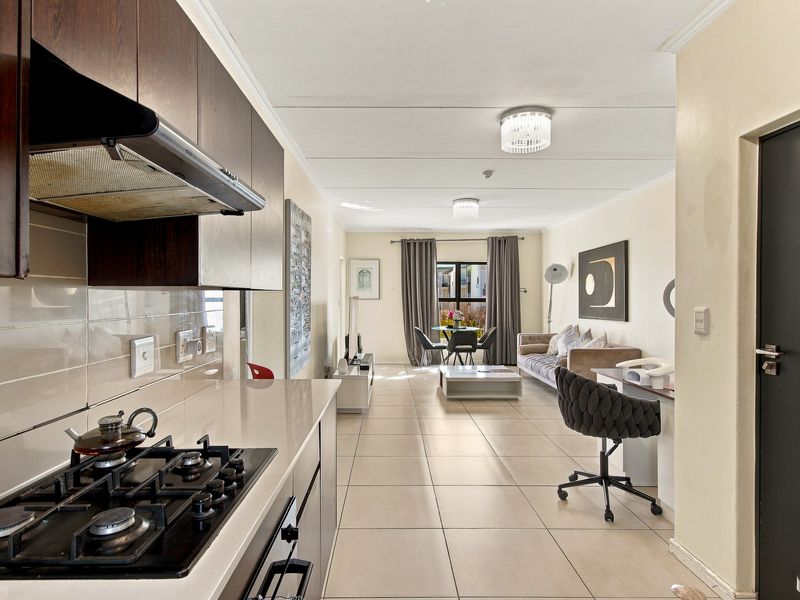 Open-plan living area featuring a modern kitchen with gas hob, stone countertops, and tiled flooring, flowing into a bright, spacious lounge area.