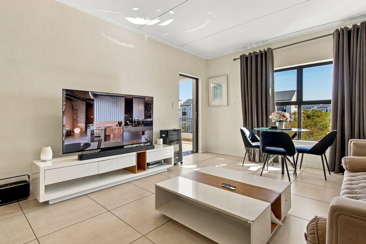 A bright and well-maintained living area featuring neutral tiled flooring, large windows for natural light, and direct access to an outdoor balcony.