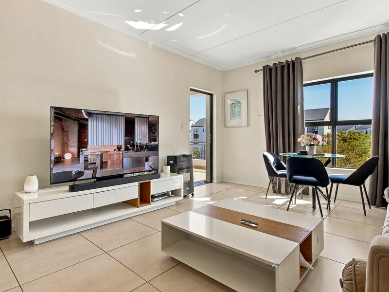 A bright and well-maintained living area featuring neutral tiled flooring, large windows for natural light, and direct access to an outdoor balcony.