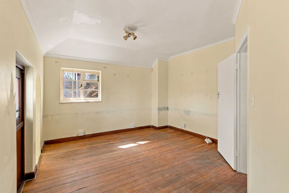 An empty bedroom featuring original timber flooring, coved cornicing, and a casement window, requiring cosmetic updates to the wall finishes.