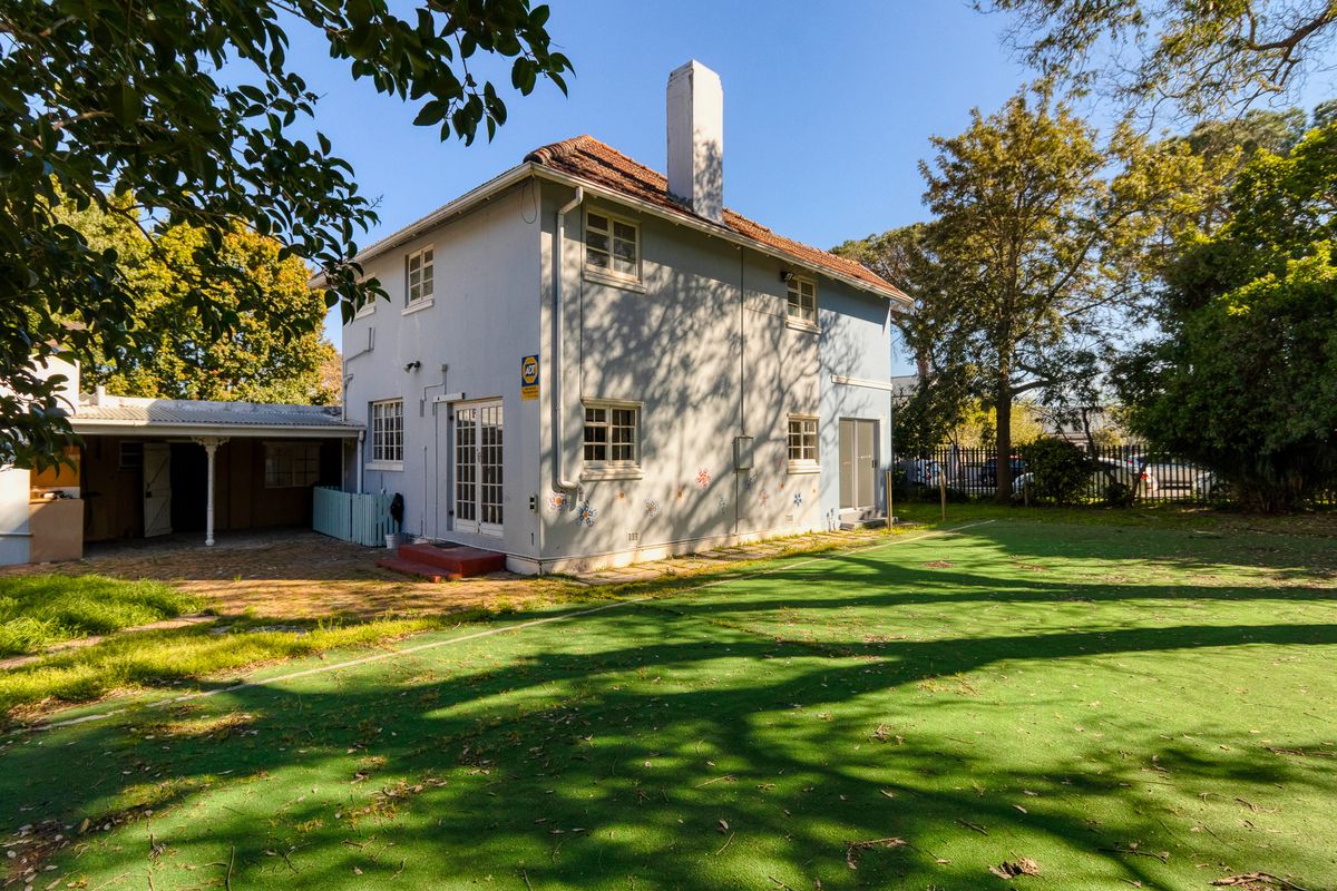 Rear view of a two-story house featuring a chimney, covered patio area, and a spacious garden with mature trees.