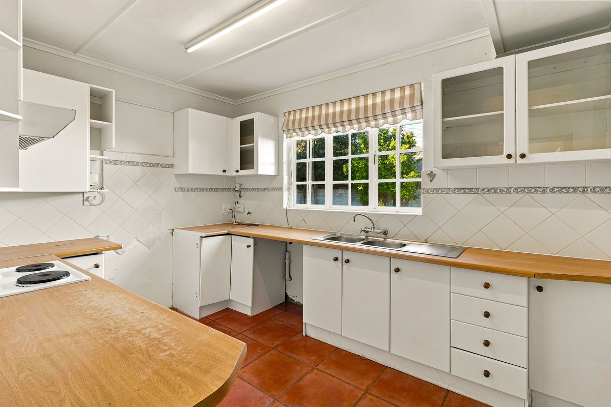 A functional kitchen featuring white cabinetry, laminate countertops, a double sink, and terracotta floor tiles, offering a blank canvas for potential renovation.