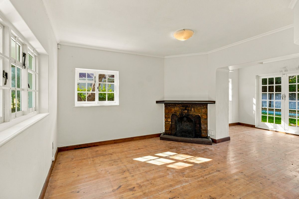 Bright living room featuring original timber flooring, a character stone fireplace, and french doors leading to the garden area.