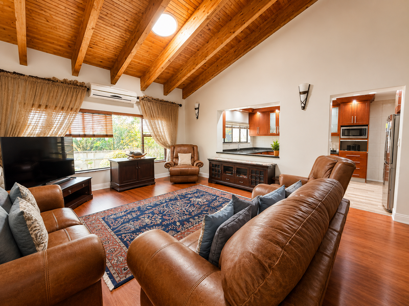 Spacious living room featuring high vaulted timber ceilings, a skylight, and a convenient pass-through window connecting to the adjacent kitchen area.