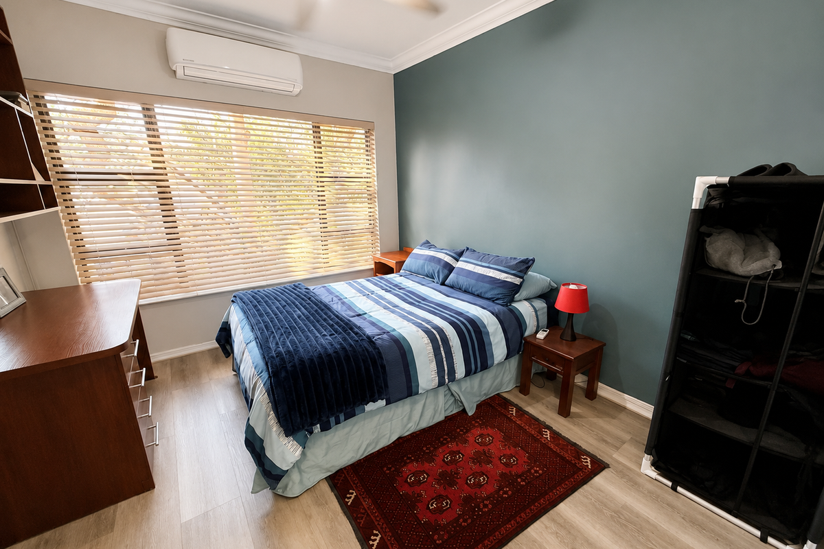 A well-maintained bedroom featuring laminate flooring, a split-system air conditioner, ceiling fan, and timber venetian blinds, accented by a feature wall.