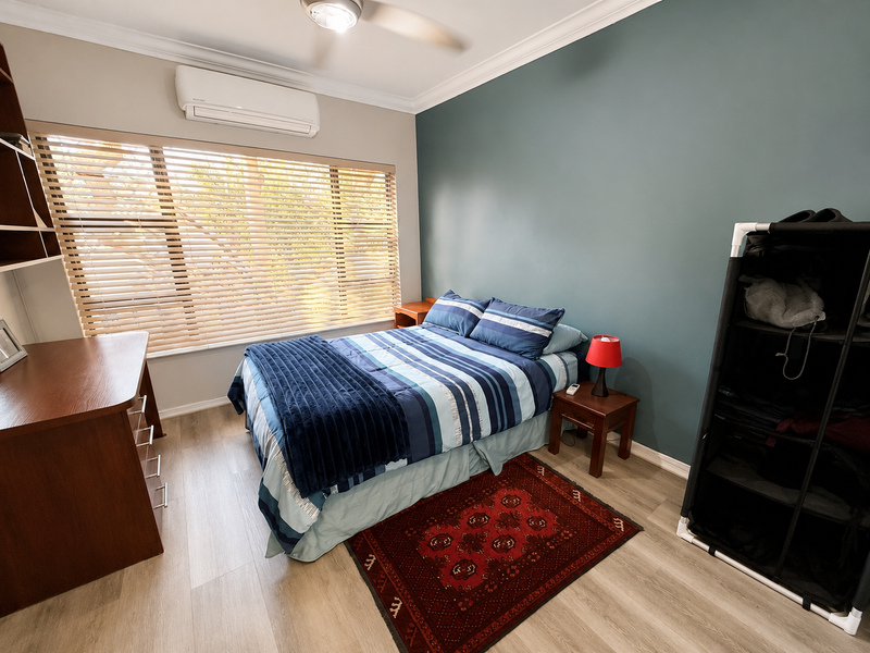 A well-maintained bedroom featuring laminate flooring, a split-system air conditioner, ceiling fan, and timber venetian blinds, accented by a feature wall.