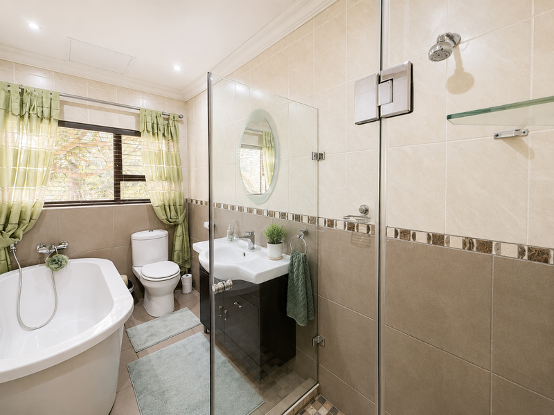 A well-maintained bathroom featuring a freestanding bathtub, a separate glass-enclosed shower, a modern vanity cabinet, and neutral-toned wall and floor tiling.