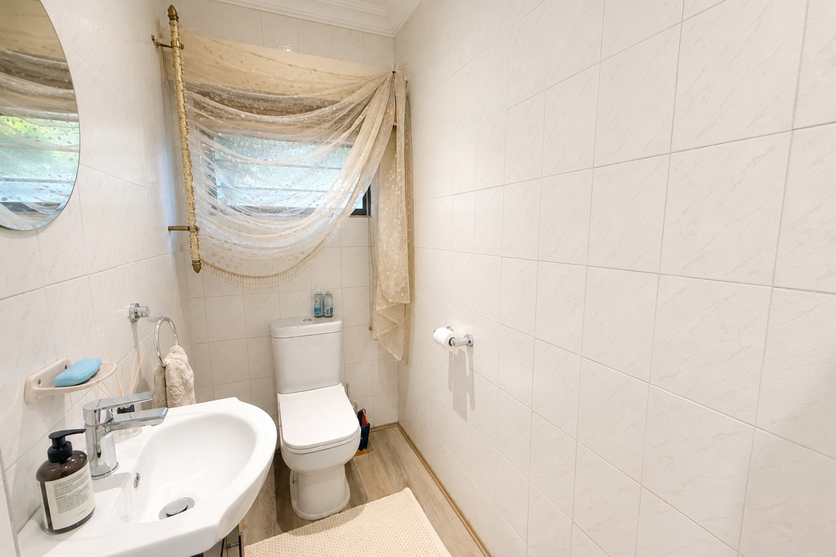 A compact bathroom featuring white wall tiles, a modern pedestal washbasin with chrome fixtures, and a dual-flush toilet.