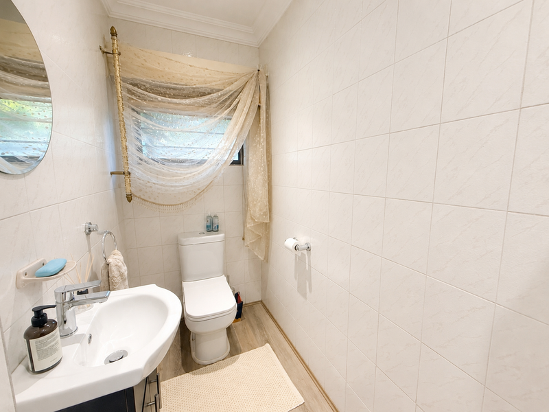 A compact bathroom featuring white wall tiles, a modern pedestal washbasin with chrome fixtures, and a dual-flush toilet.