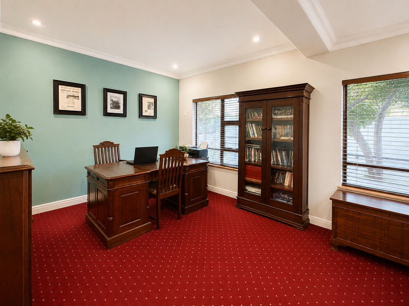 A well-maintained home office featuring red carpeting, a teal accent wall, recessed lighting, and built-in wooden cabinetry with large windows.