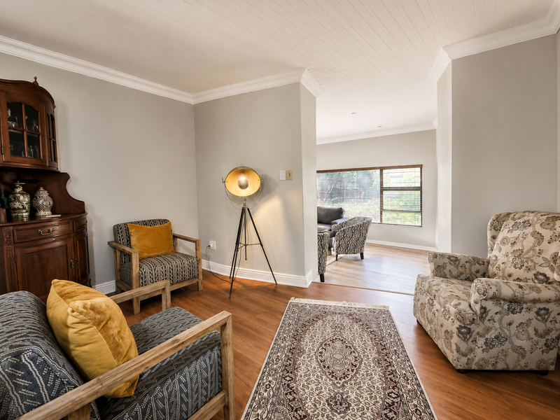 A well-maintained living area featuring laminate flooring, classic cornicing, and a tongue and groove ceiling, flowing into an adjacent lounge space.