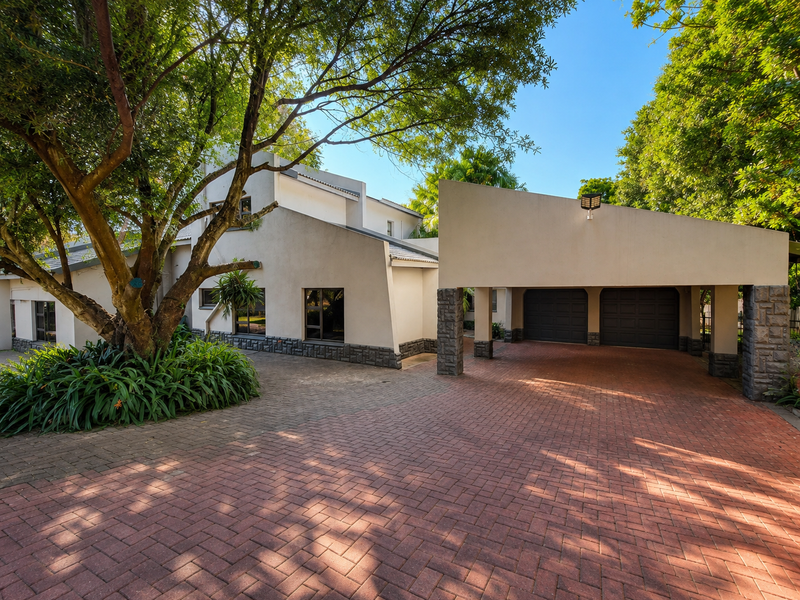 Front view of the property featuring a paved driveway, double garage, and mature landscaping with stone-clad architectural details.
