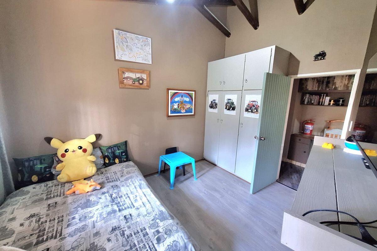 A bedroom featuring exposed timber ceiling beams, laminate flooring, and a built-in wardrobe with an adjacent small storage or utility area.