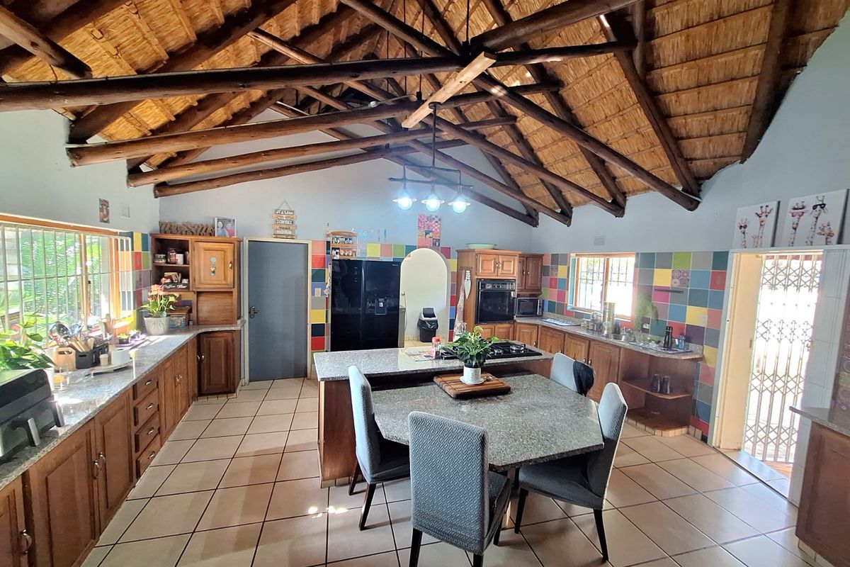 Spacious kitchen featuring a high vaulted thatched ceiling with exposed timber rafters, granite countertops, and extensive timber cabinetry.