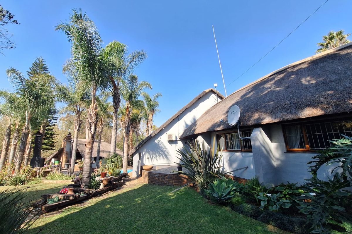 Rear view of the property featuring a traditional thatch roof, landscaped garden, brick patio area, and established palm trees.