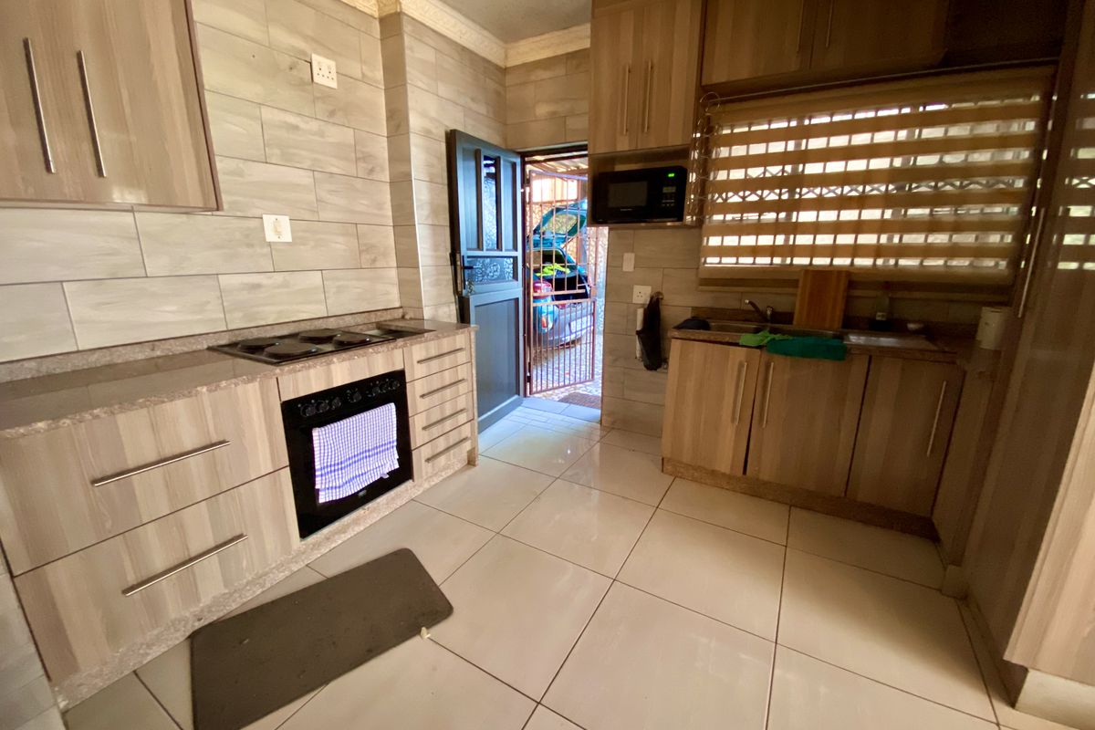 A functional kitchen featuring wood-look cabinetry, stone countertops, built-in oven and hob, and tiled flooring with direct access to the exterior.