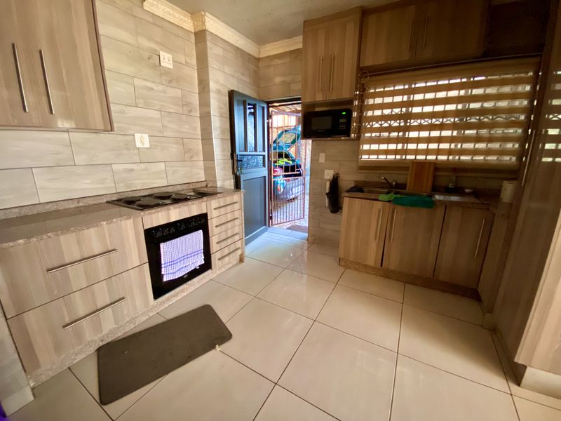 A functional kitchen featuring wood-look cabinetry, stone countertops, built-in oven and hob, and tiled flooring with direct access to the exterior.