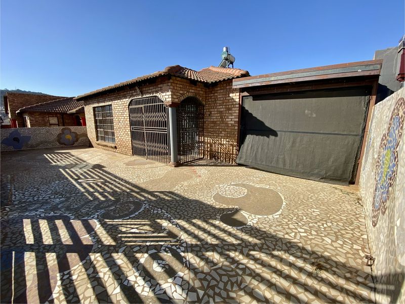 Front exterior view of a brick house featuring a mosaic paved driveway, security gates, and a garage with a shade cloth cover.