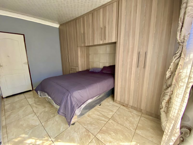 Bedroom featuring extensive built-in wooden cupboards with integrated headboard space and neutral tiled flooring.