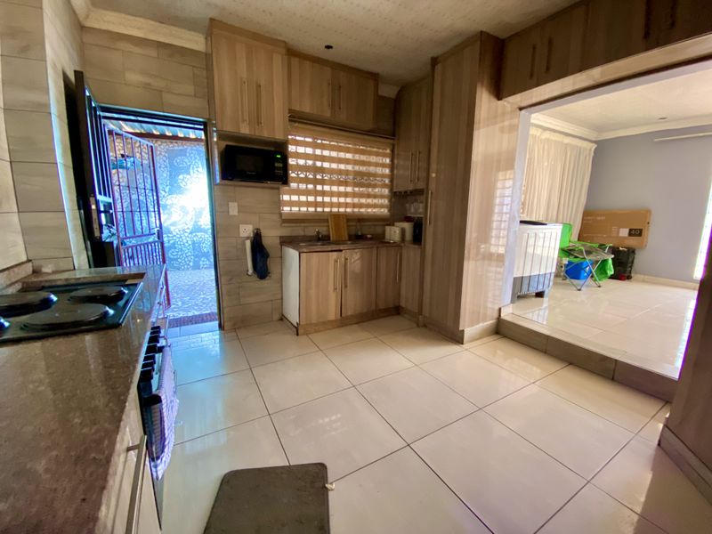 A functional kitchen featuring wood-finish cabinetry, stone countertops, and an integrated hob, with direct access to an outdoor area and adjacent living space.